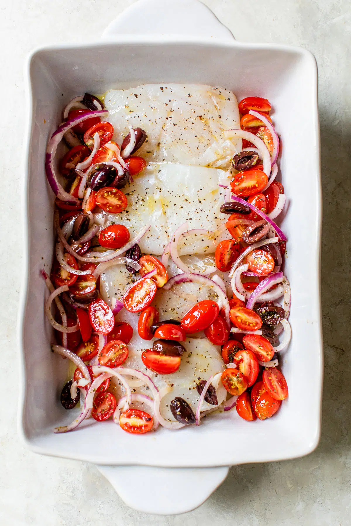 raw cod fillets in a baking dish topped with grape tomatoes