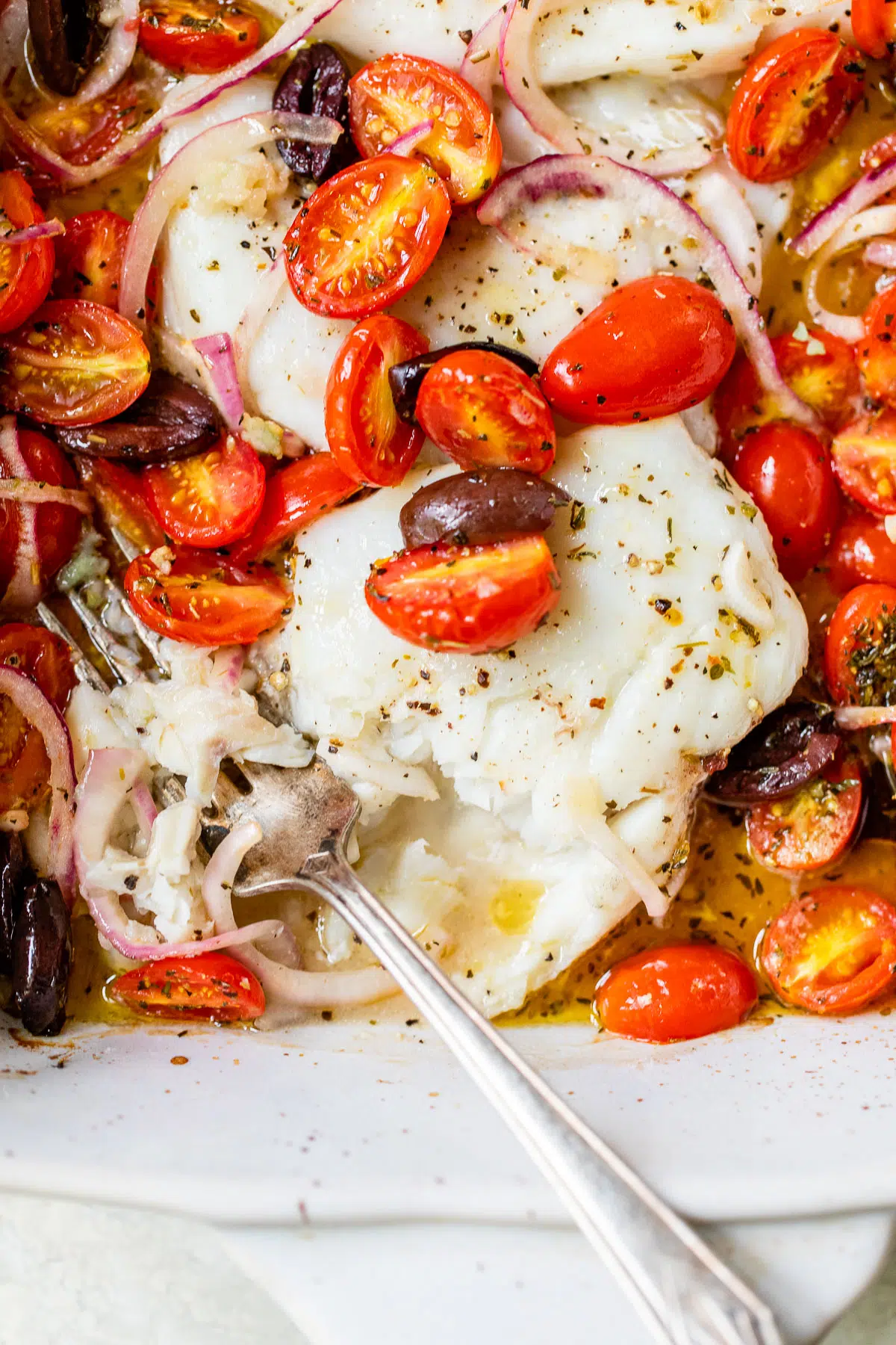 flakey baked cod in a baking dish with tomatoes, onion and olives