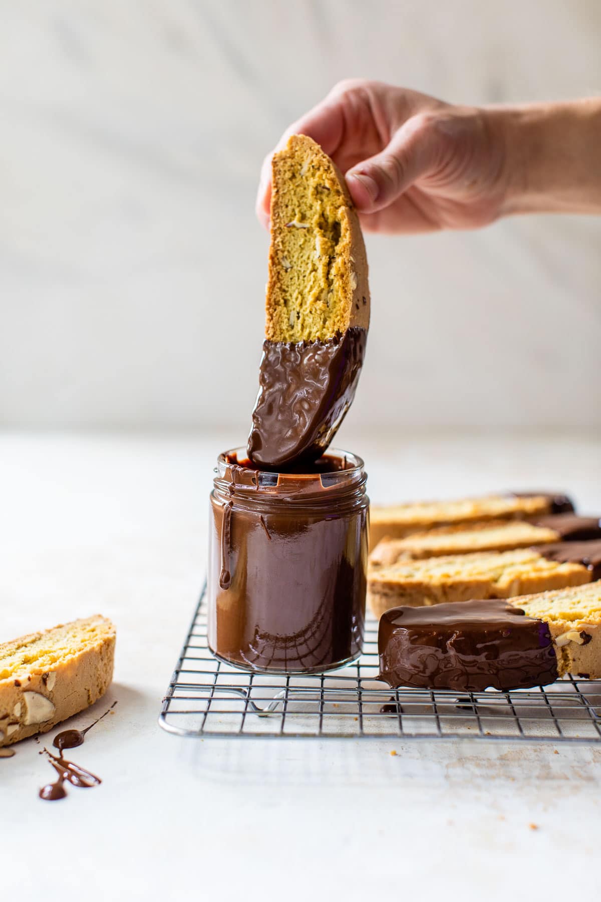 someone dipping a piece of biscotti in a jar of melted chocolate