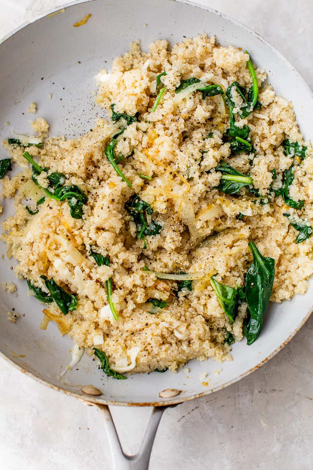 quinoa, onions and spinach in a white skillet