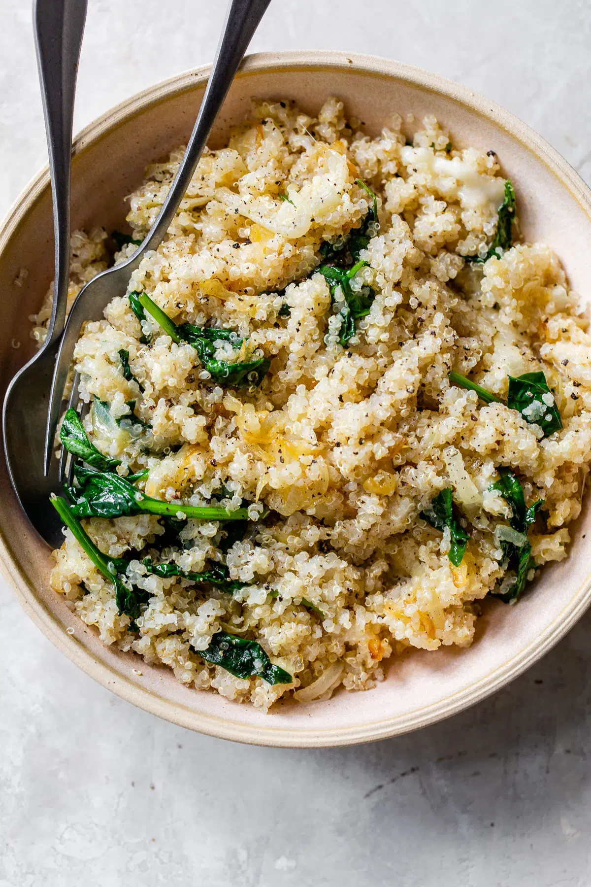 cooked quinoa, spinach and caramelized onions in a pink bowl