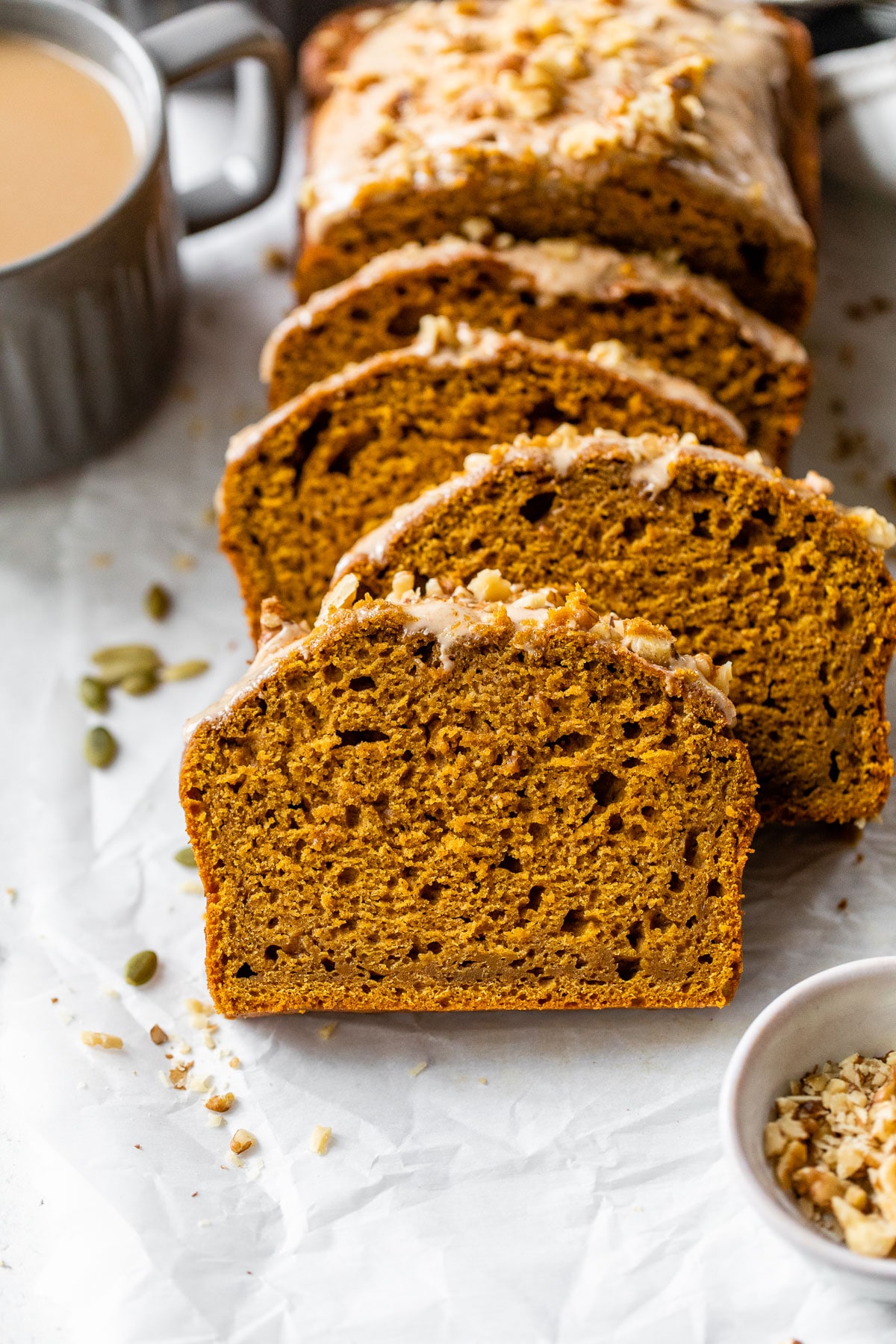 sliced pumpkin bread on parchment paper beside a mug of coffee