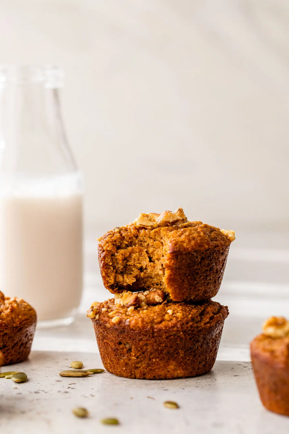two pumpkin muffins stacked on top of one another beside a tall glass of milk