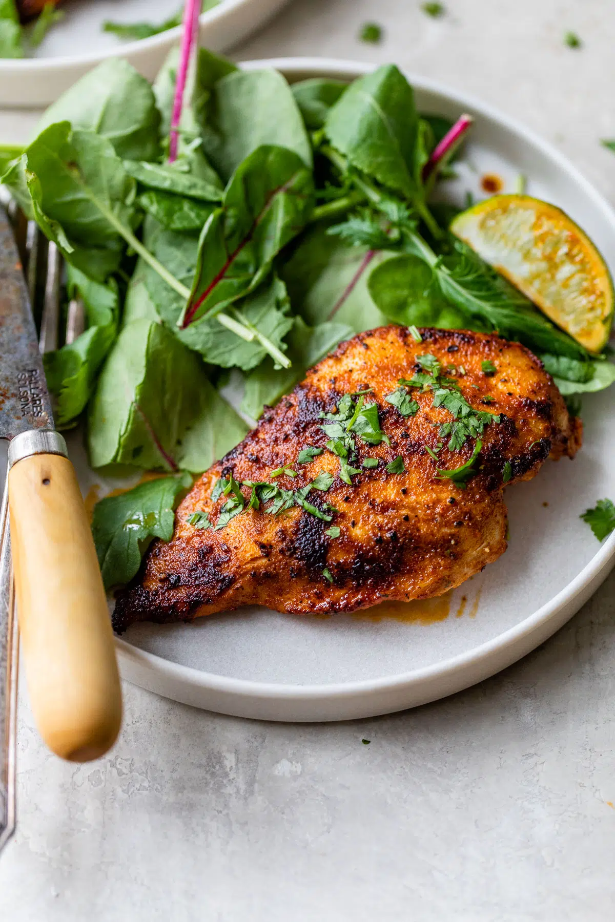 charred chicken breast on a plate beside a handful of lettuce
