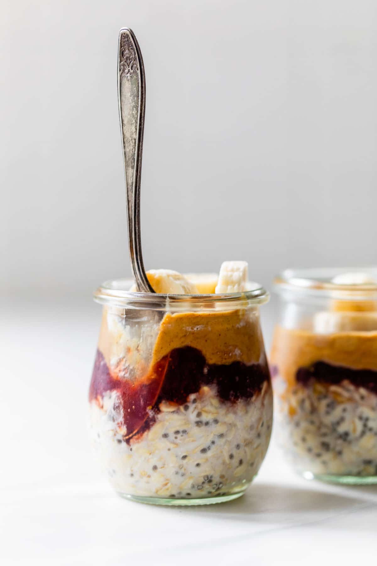 a jar of oats, peanut butter and jelly with a spoon in it