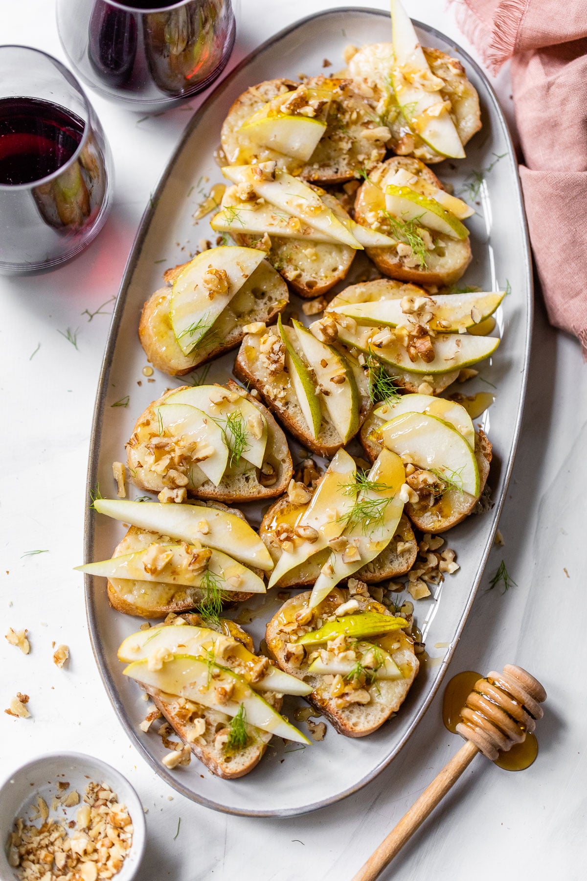 a platter with pear crostini on it beside two glasses of red wine