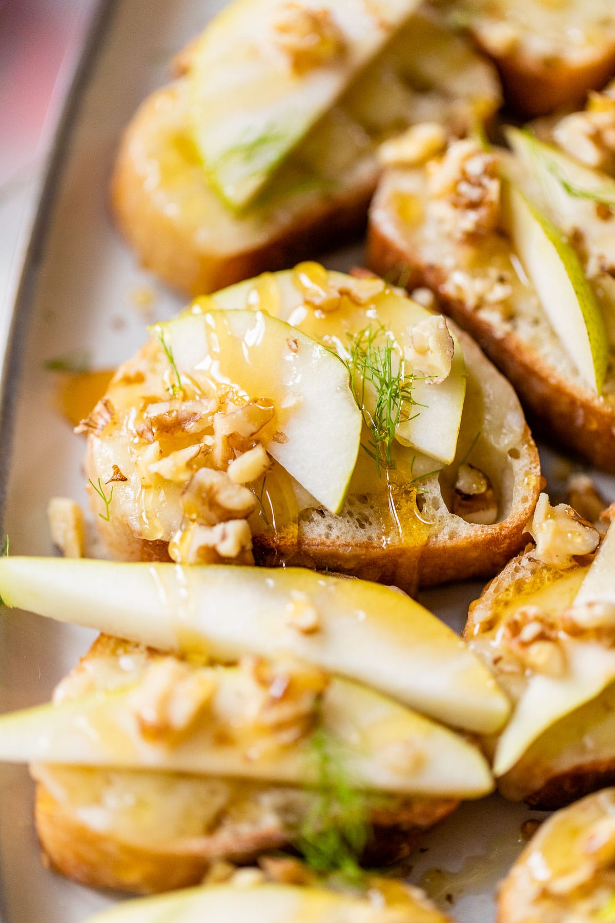 a small slice of bread on a plate topped with pears, walnuts and honey