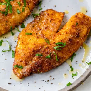 cooked breaded fish on a plate topped with chopped parsley