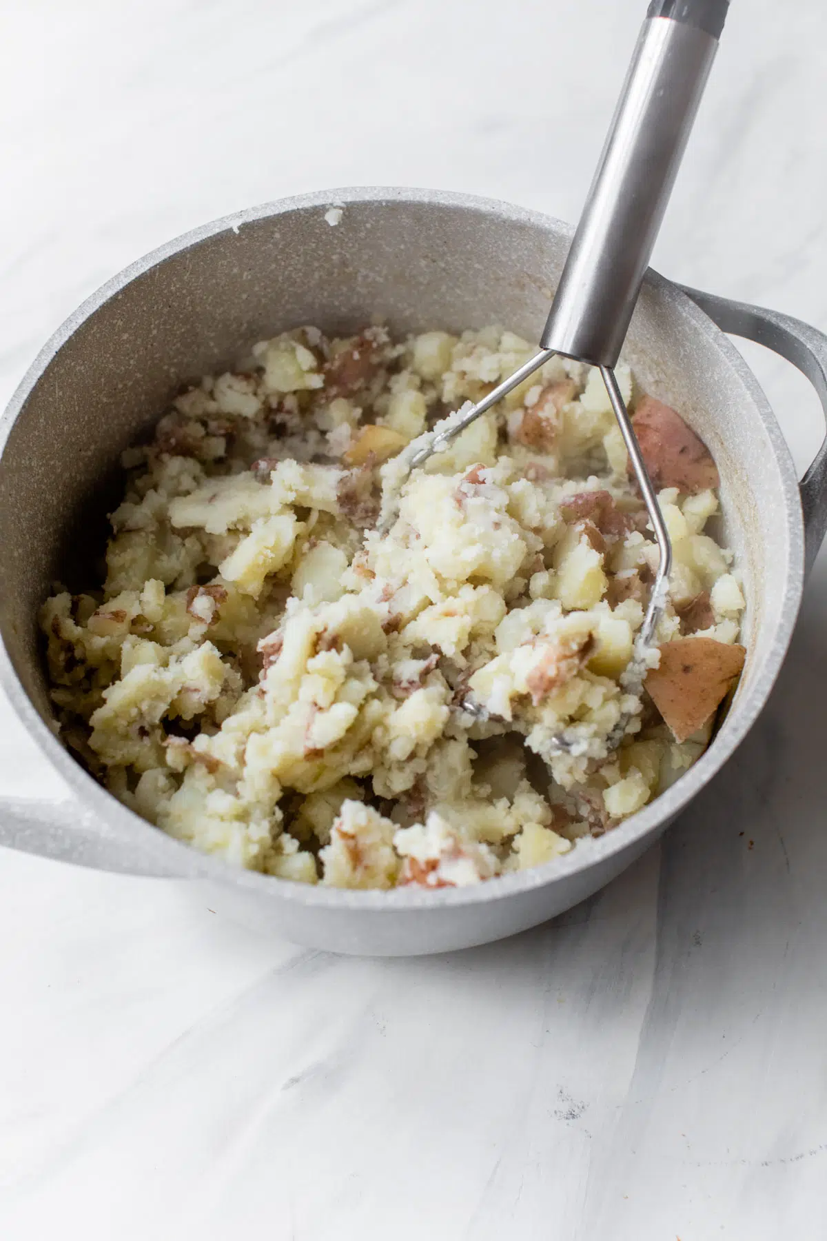 mashed potatoes in a pot with a potato masher