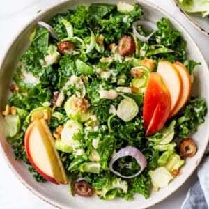 a bowl of kale salad with apples, brussels sprouts and shallots