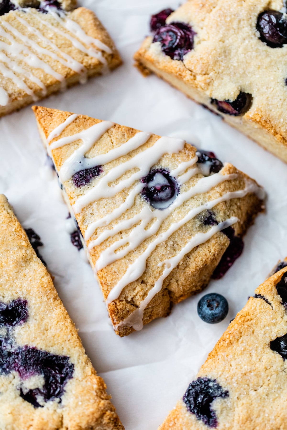 blueberry scones drizzled in a glaze on parchment paper