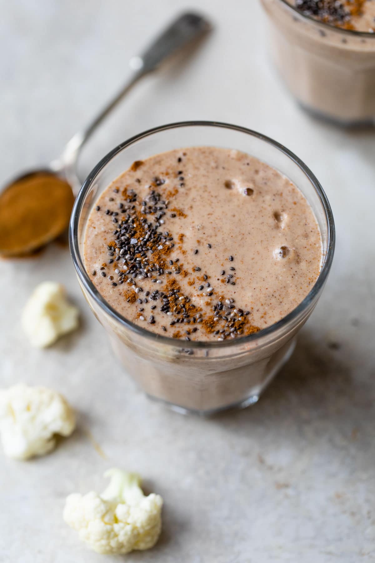 smoothie in a glass topped with cinnamon and chia seeds beside a spoon of almond butter