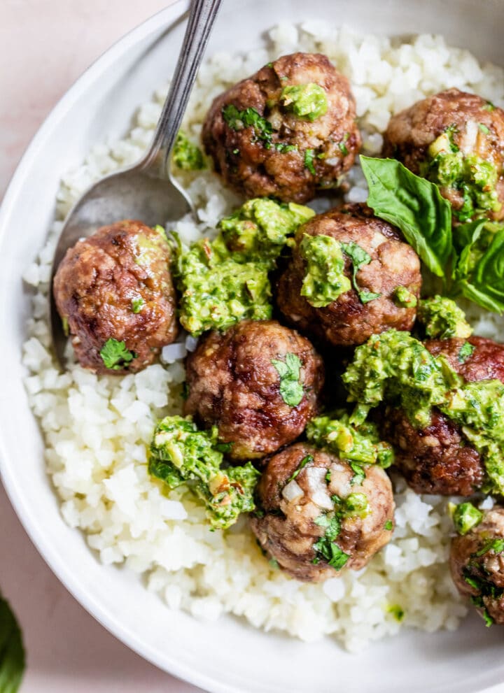 cauliflower rice in a bowl topped with meatballs and pesto