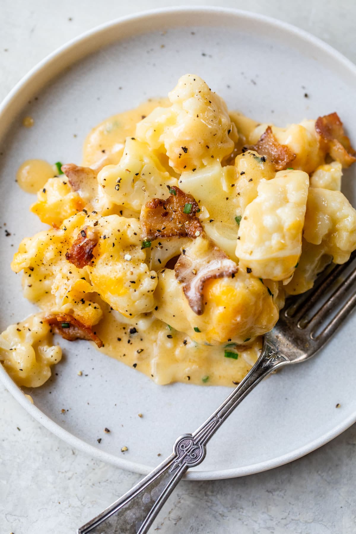 cauliflower and bacon covered in cheese on a plate with a fork