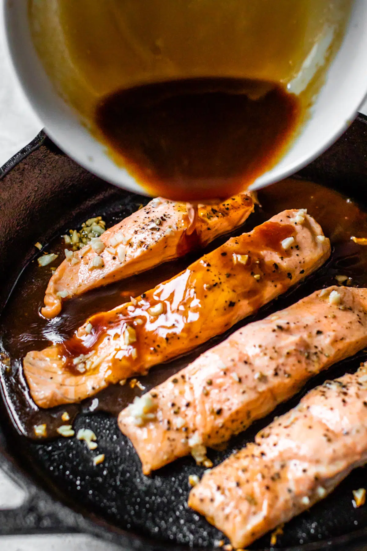 someone pouring soy sauce into a skillet with salmon and minced garlic