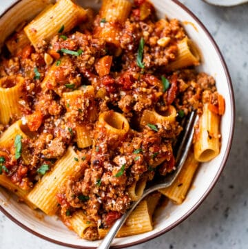 rigatoni in a bowl coated in bolognese sauce