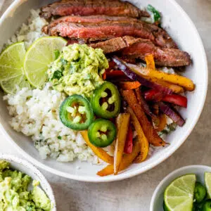 a bowl filled with cauliflower rice, steak, peppers, and guacamole