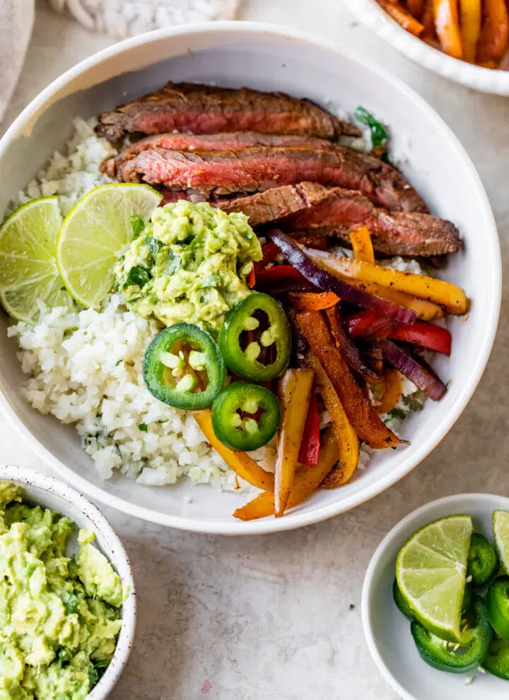 a bowl filled with cauliflower rice, steak, peppers, and guacamole