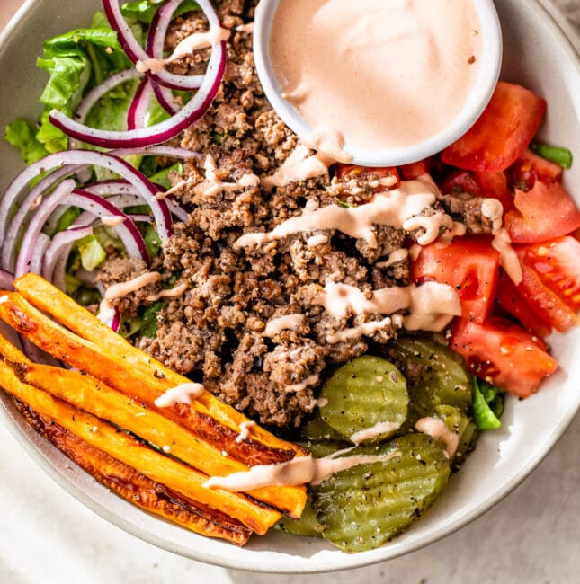 bowl filled with lettuce, ground beef, sweet potato, tomato and pickles