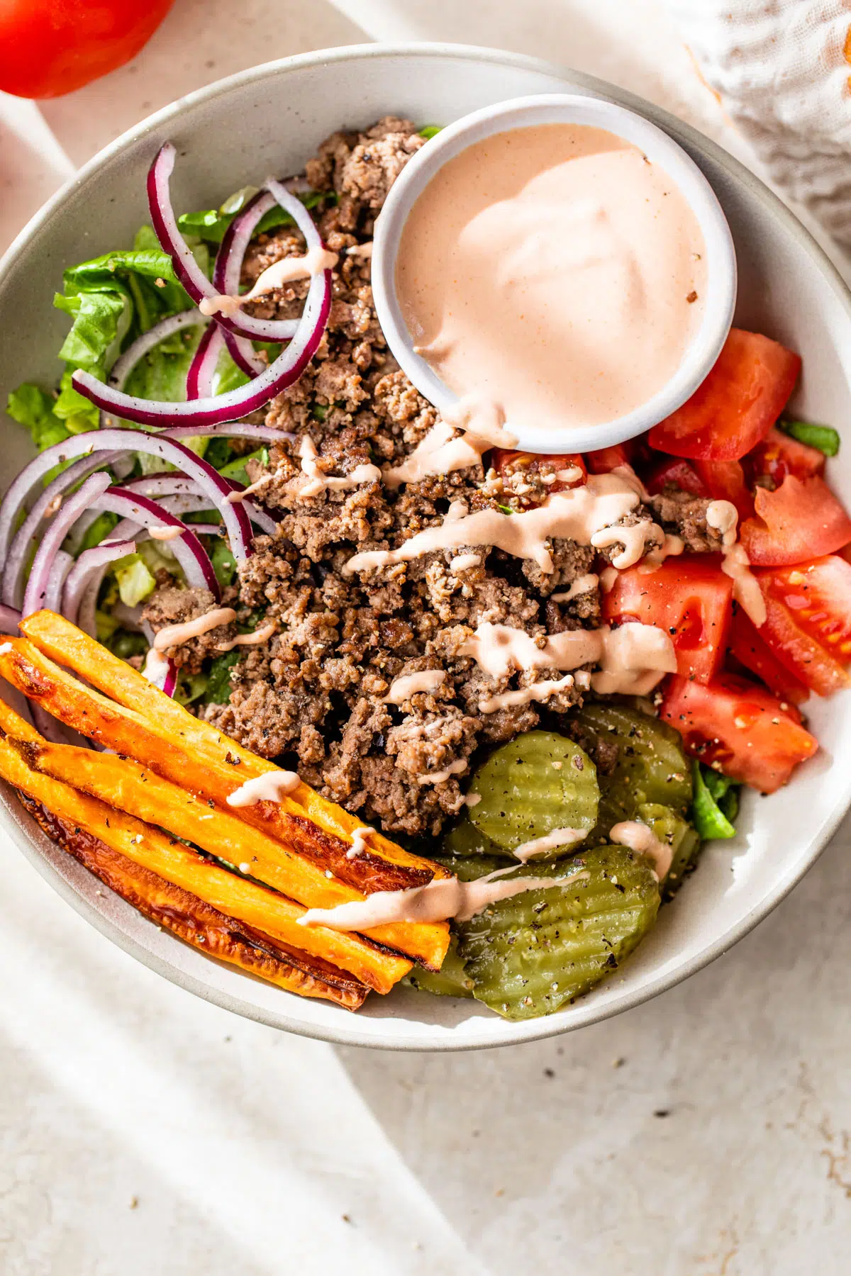 bowl filled with lettuce, ground beef, sweet potato, tomato and pickles