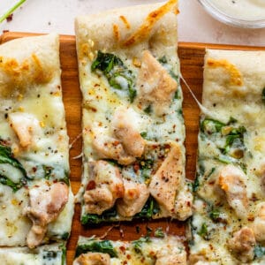 sliced pizza on a cutting board topped with cheese, spinach and chicken