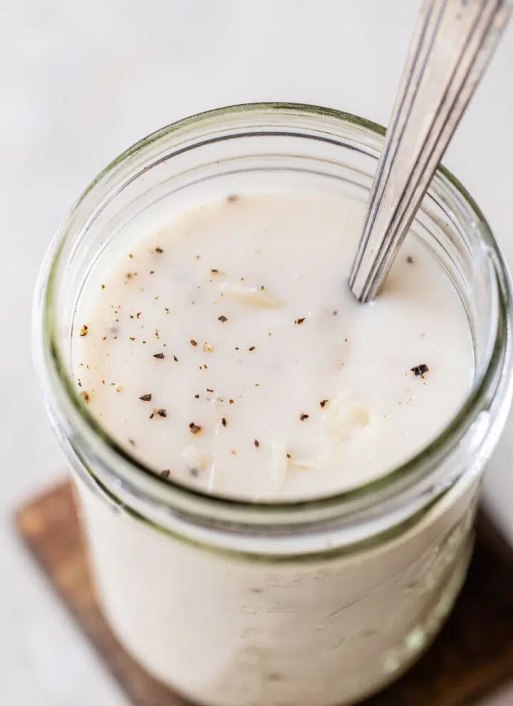 creamy white sauce in a glass jar sprinkled with black pepper