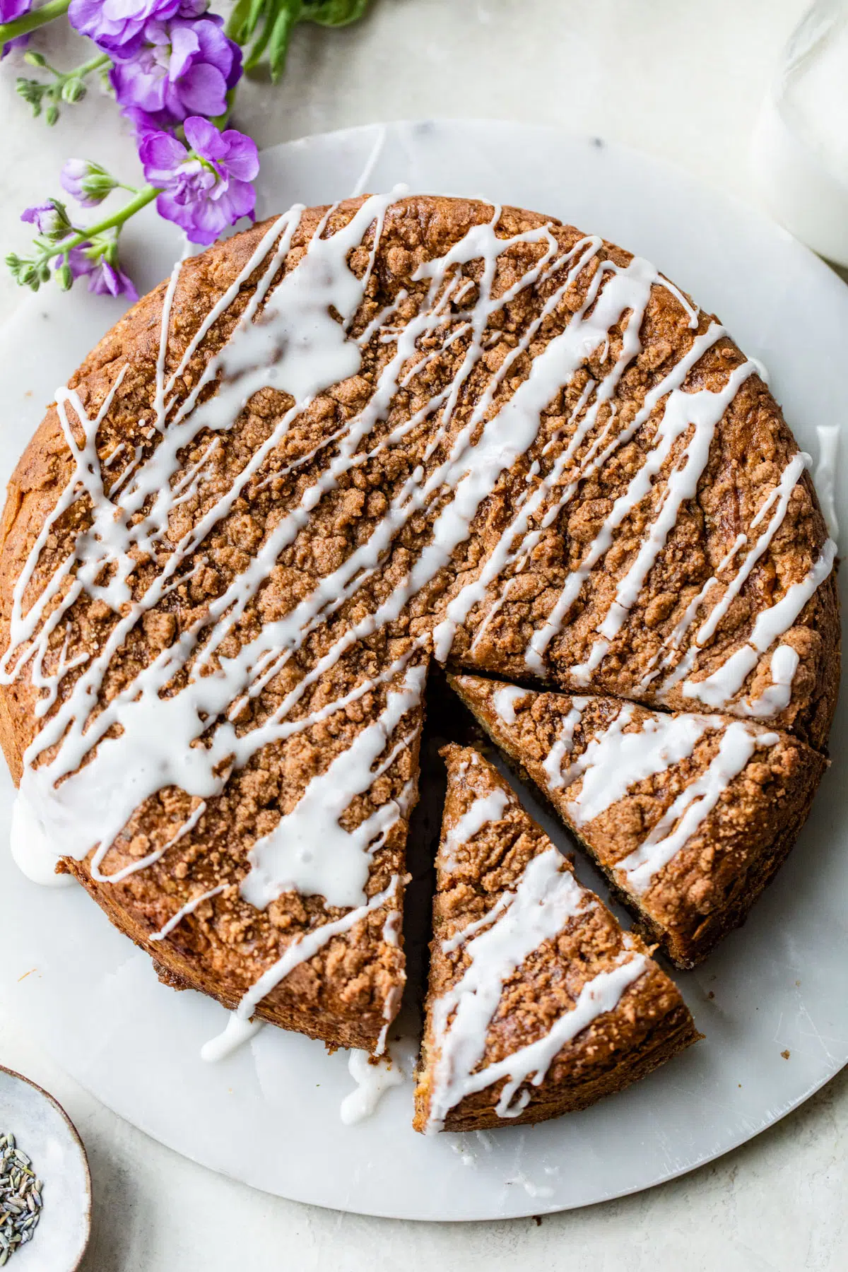 coffee cake on a round platter cut into slices and drizzled with a glaze