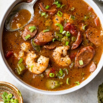 a bowl of gumbo with shrimp and sausage beside a small bowl of green onions