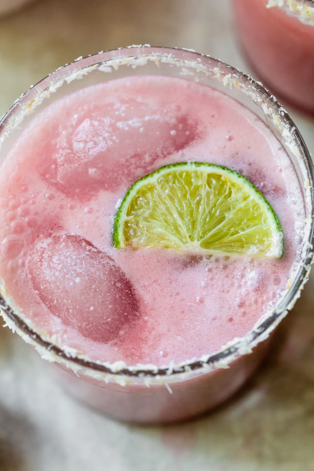 close up photo of a pink-colored cocktail with a lime wedge in it