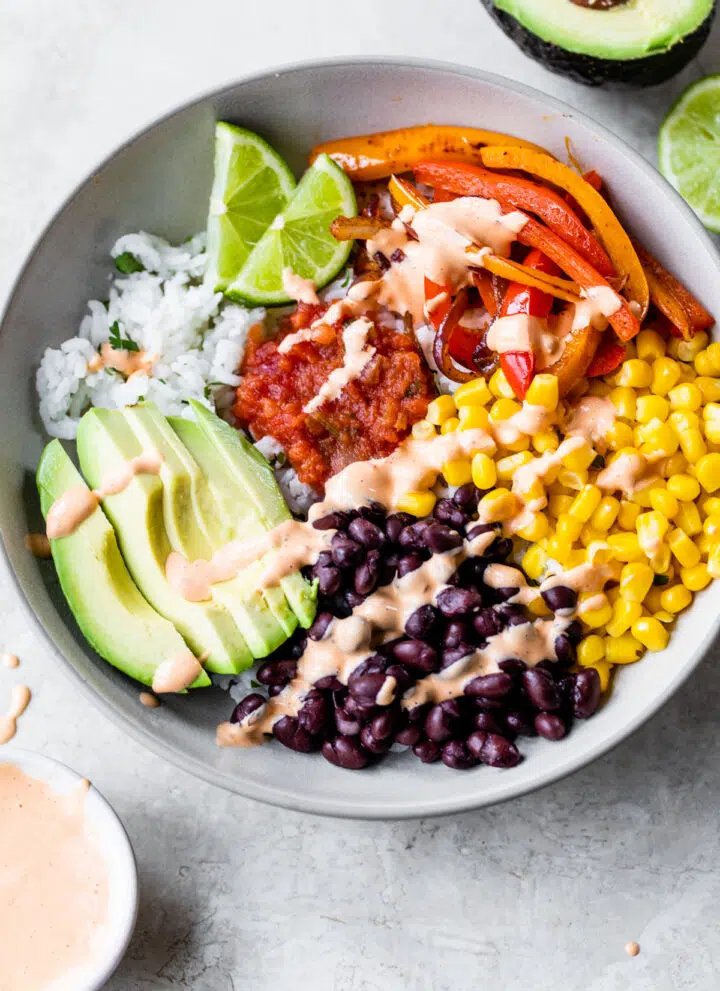 bowl of rice topped with black beans, corn, peppers, avocado, salsa, and chipotle aioli
