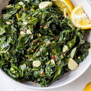 greens cooked in a bowl with garlic and lemon wedges