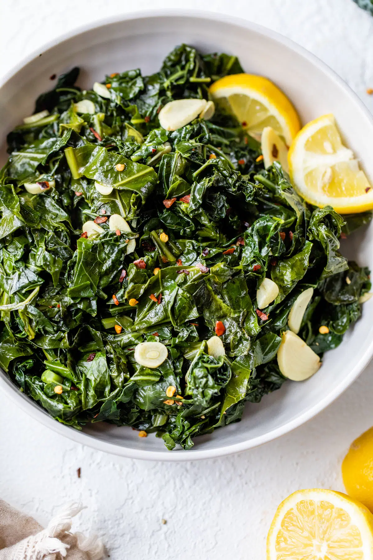 cooked greens in a bowl with garlic and lemon wedges