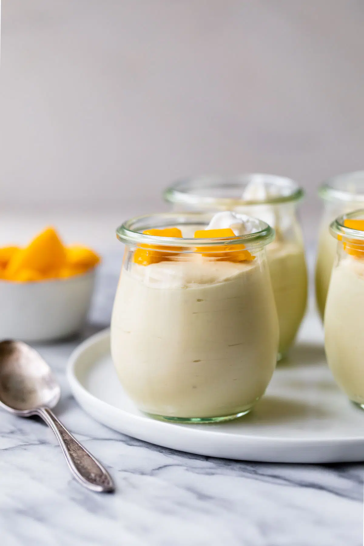 mango mousse in jars beside a small bowl of mangos