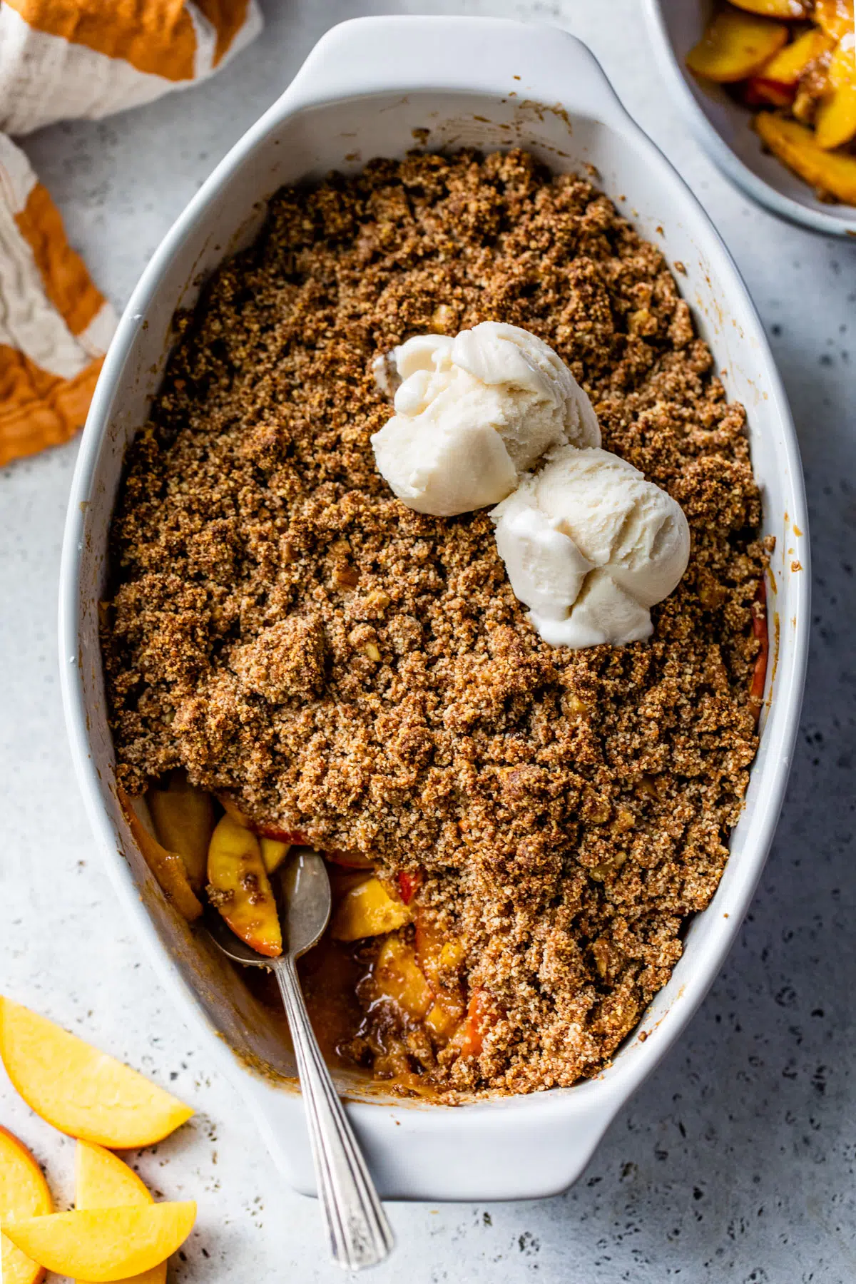 baked peaches in a dish topped with a crumb topping and vanilla ice cream