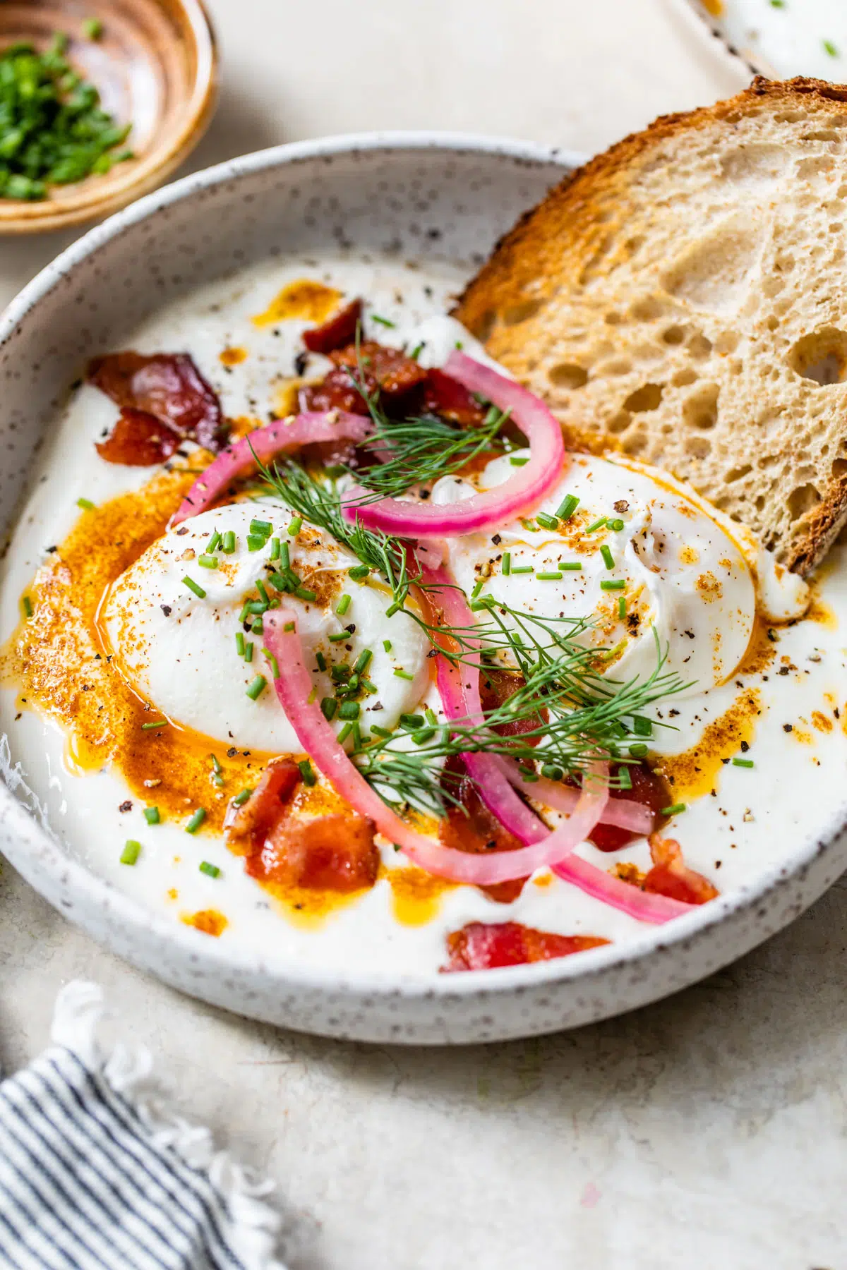 yogurt in a bowl topped with eggs, bacon, red onion, herbs, and toast