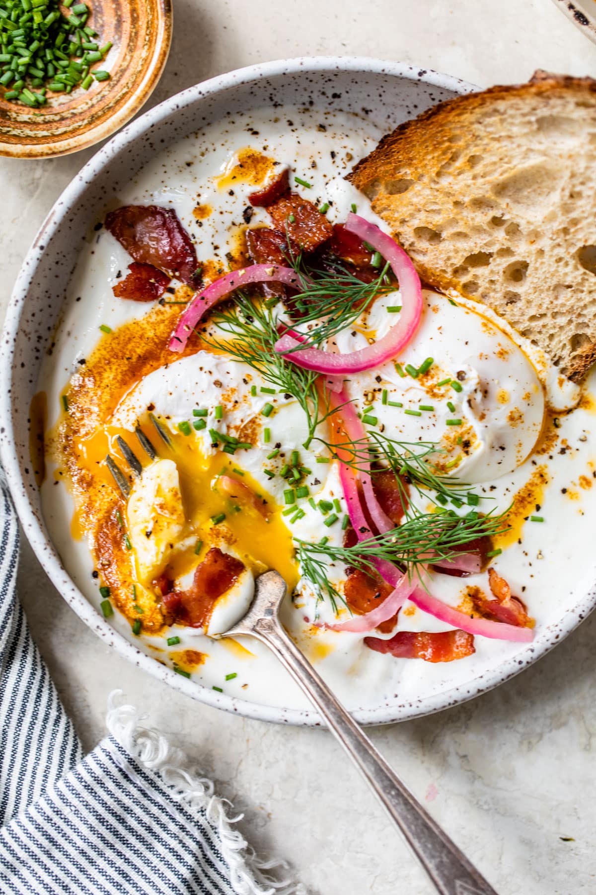 a large bowl of yogurt topped with poached eggs, bacon and fresh herbs