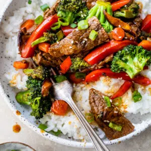 a bowl of rice topped with beef and vegetables like broccoli and red bell pepper