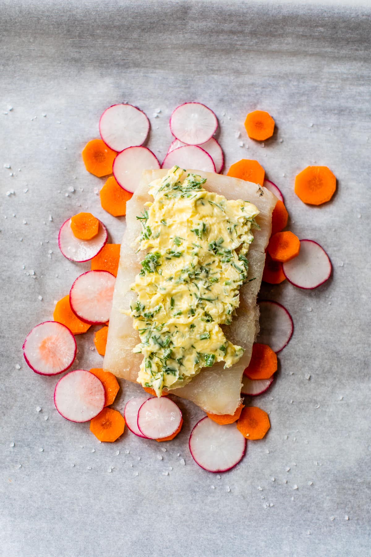 a piece of white fish topped with butter and on top of carrots and radishes