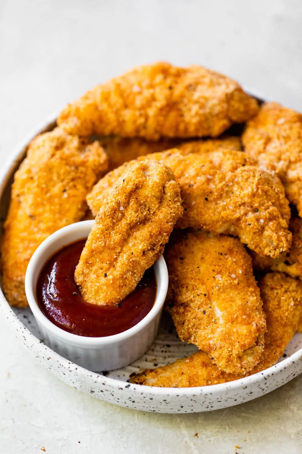 bowl of chicken tenders and one of them being dipped in ketchup