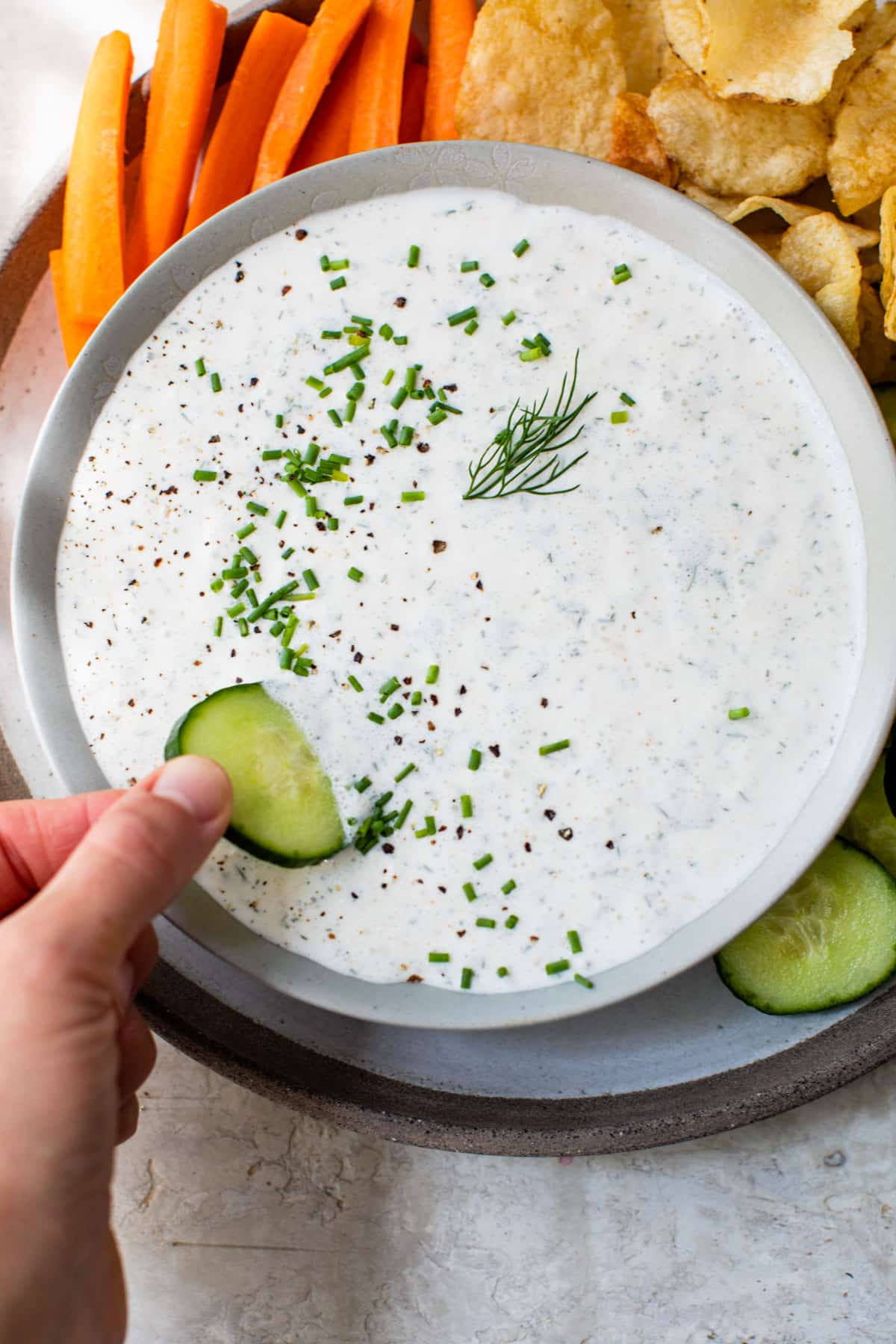 someone's hand dipping a cucumber into a bowl of white-colored dip