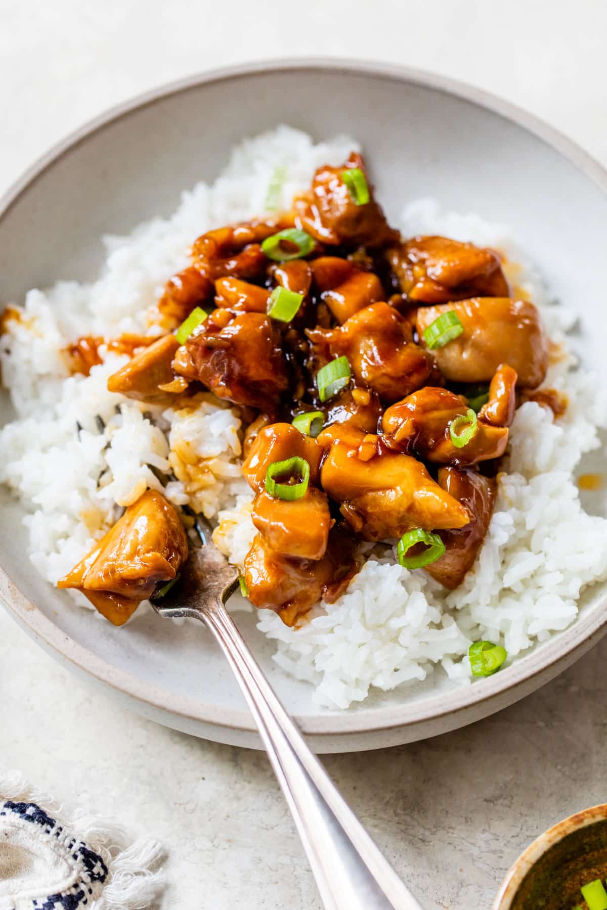orange glazed chicken in a bowl over white rice and topped with green onions