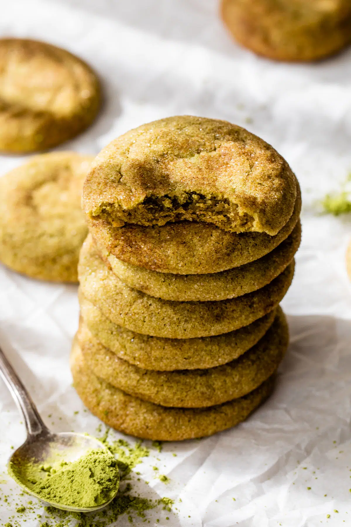a stack of snickerdoodle cookies on parchment paper beside a spoon of matcha powder