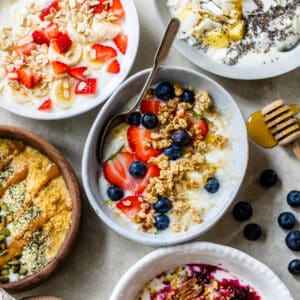 five different yogurt bowls topped with various toppings like fruit, nuts and oats