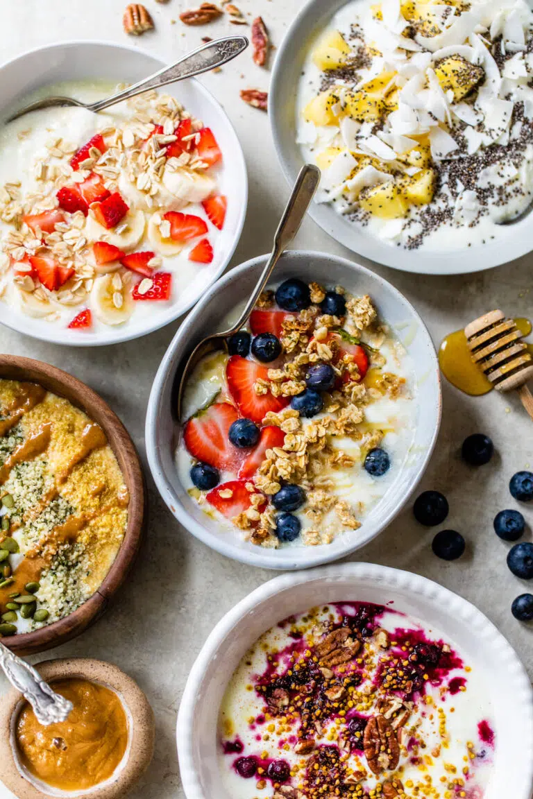 five different yogurt bowls topped with various toppings like fruit, nuts and oats