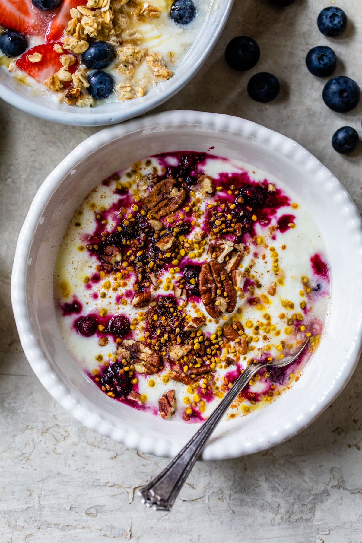a bowl of yogurt with a blueberry compote swirl, bee pollen and pecans