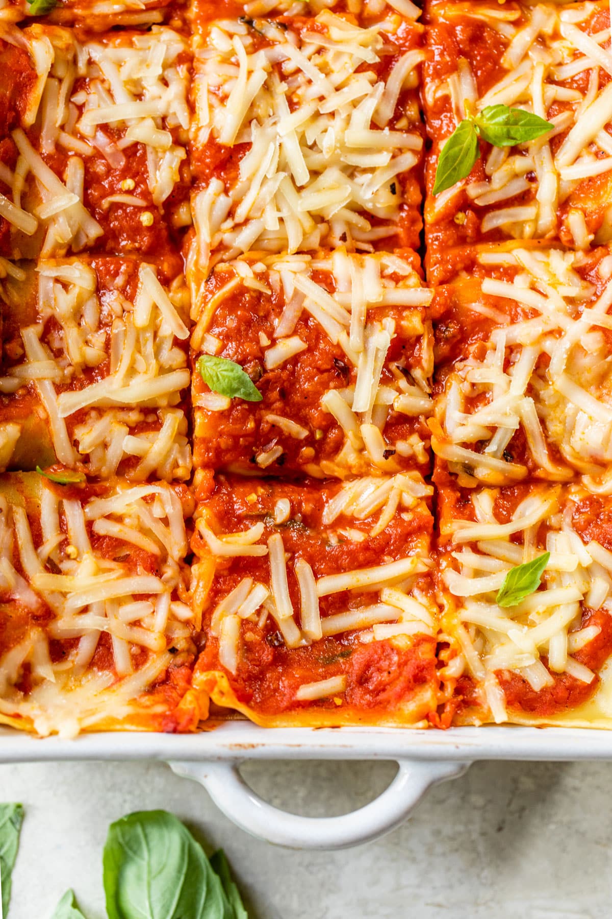 a baking dish of lasagna topped with shredded cheese and fresh basil