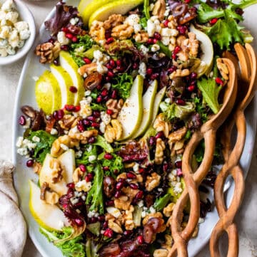 mixed greens on a platter topped with sliced pear, walnuts and pomegranate