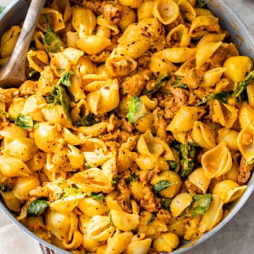 skillet filled with pasta shells, sausage and spinach with a wooden spoon