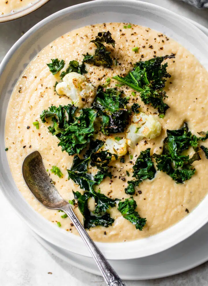 a bowl of creamy yellow-colored soup topped with cauliflower florets and kale chips