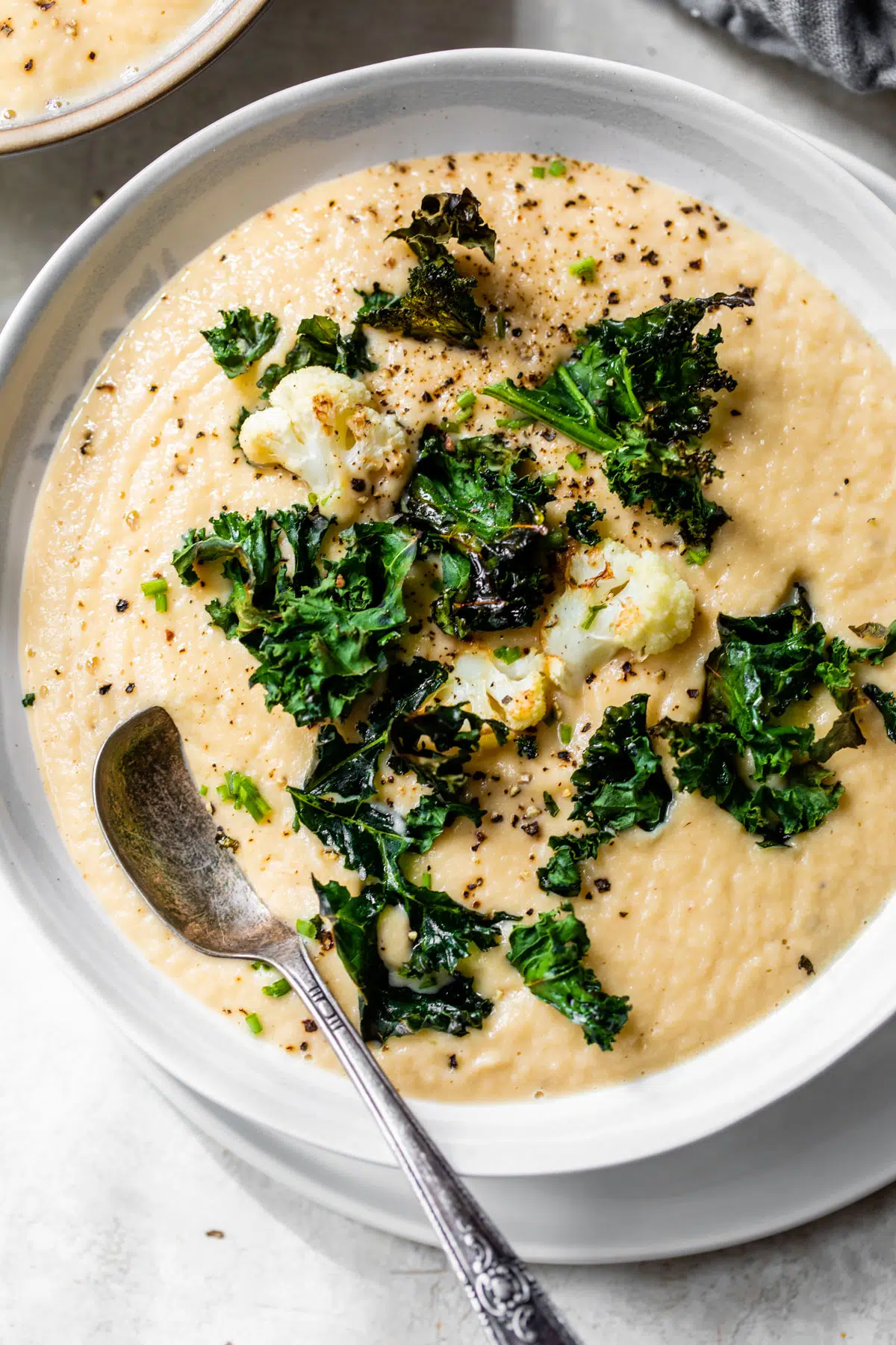 a bowl of creamy yellow-colored soup topped with cauliflower florets and kale chips